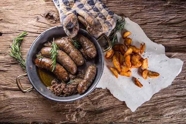 Embutidos. Chorizo de cerdo asado en una sartén con patatas y romero.