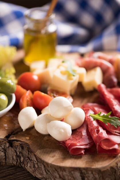 Embutidos surtidos y un plato de queso, sobre una tabla de cortar de madera. Antipasti italiano