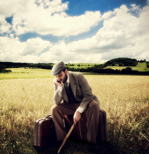 Foto emigrante en el campo sentado en maletas de cartón