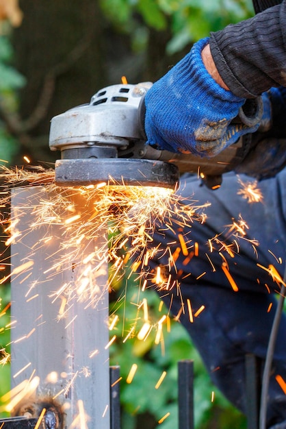 Foto se emiten muchas chispas calientes mientras el artesano trabaja cortando el poste de metal con una fresadora angular