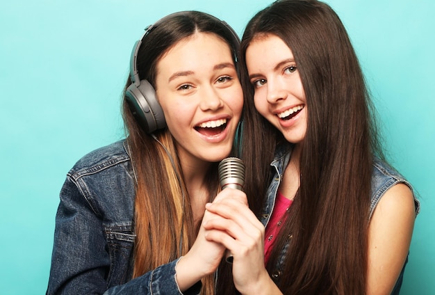 Emoción de estilo de vida y concepto de personas Dos jóvenes amigas de pie juntas y escuchando música y cantando