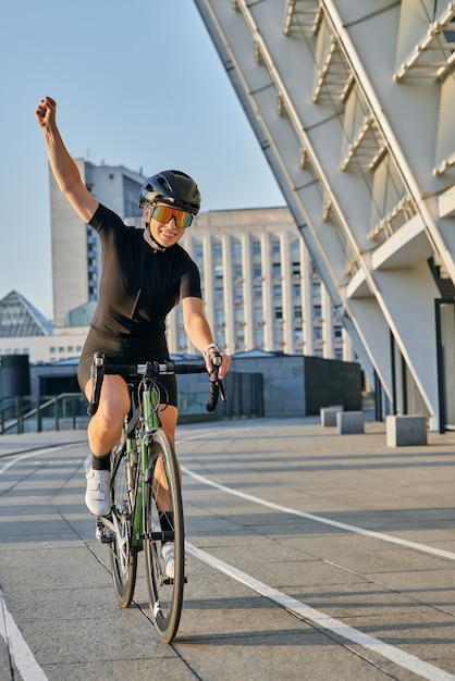 Emocionada ciclista profesional en ropa de ciclismo negra y equipo de protección sonriendo elevándola