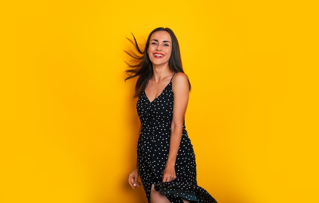 Emocionada feliz linda mujer moderna con un vestido de verano está bailando y divirtiéndose aislado sobre fondo amarillo