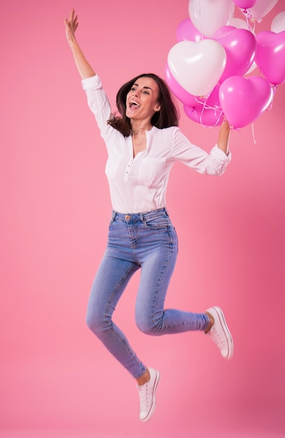 Emocionada hermosa linda mujer encantadora con globos de colores en las manos está saltando y sonriendo