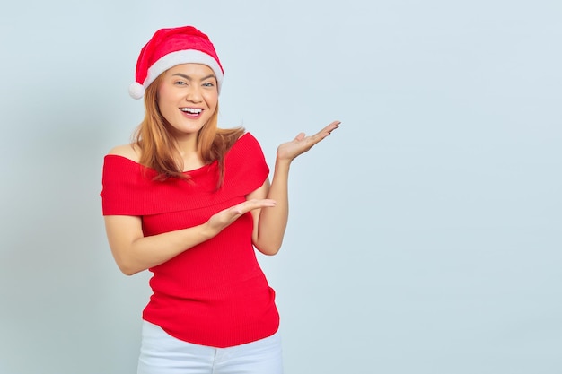 Emocionada hermosa mujer asiática con vestido de Navidad que muestra el espacio de la copia en la palma de la mano sobre fondo blanco.