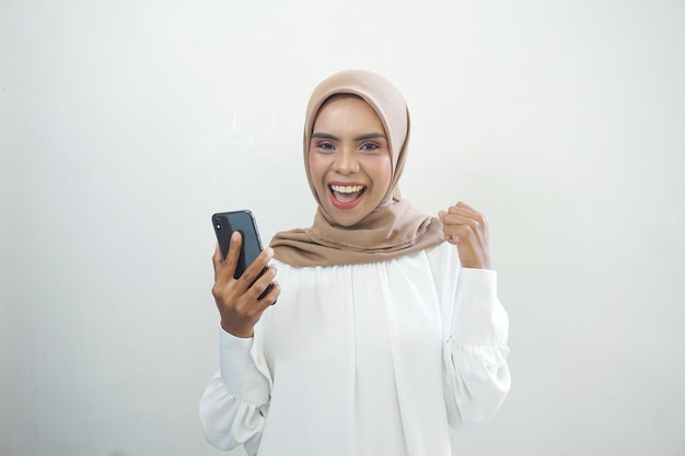 Emocionada hermosa mujer musulmana asiática mostrando teléfono móvil aislado sobre fondo blanco.