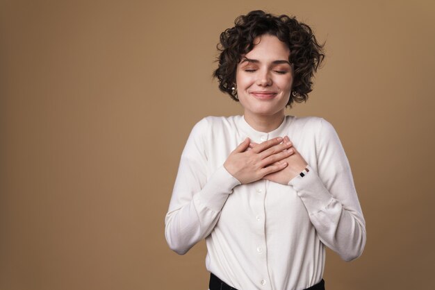 Emocionada hermosa mujer sonriendo y tomados de la mano en el pecho aislado sobre pared beige