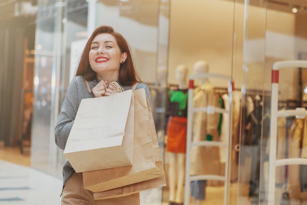 Emocionada joven bella mujer sonriendo con los ojos cerrados de placer, llevando sus bolsas de compras en el centro comercial