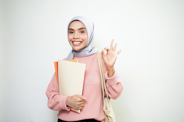 Emocionada joven estudiante musulmana asiática en suéter rosa con bolsa con libro