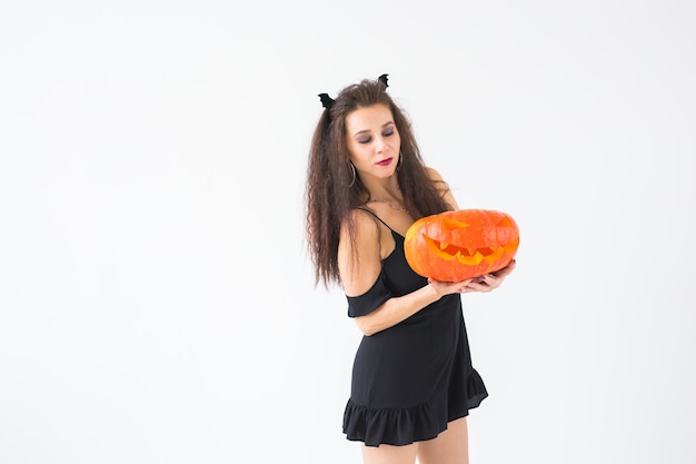 Emocionada joven feliz en traje de halloween posando con calabaza tallada sobre fondo claro con espacio de copia