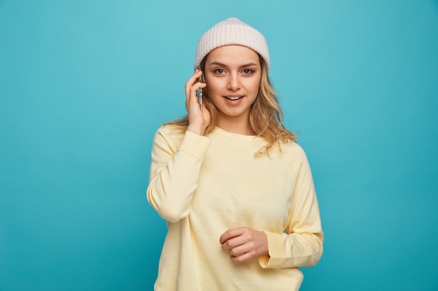 Emocionada joven vistiendo gorro de invierno hablando por teléfono