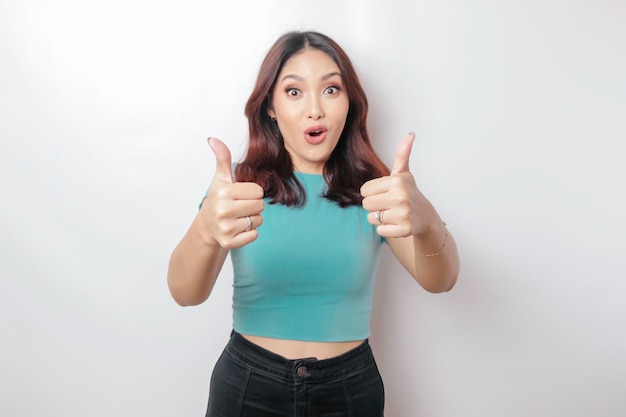 Emocionada mujer asiática con camisa azul da pulgares hacia arriba gesto de aprobación aislado por fondo blanco