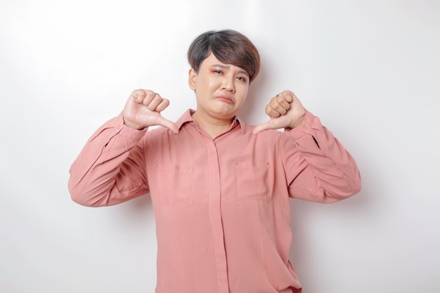 Emocionada mujer asiática de pelo corto con camisa rosa da pulgares arriba gesto de aprobación aislado por fondo blanco