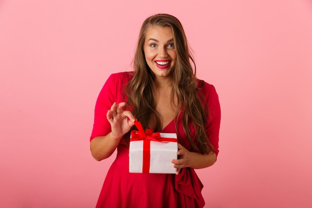 Emocionada mujer gordita de 20 años con vestido rojo sonriendo y sosteniendo la caja actual