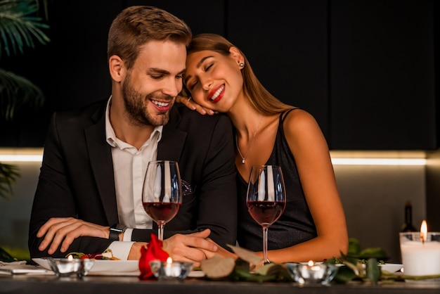 Emocionada pareja amorosa celebrando un evento especial con vino y velas cenando juntos