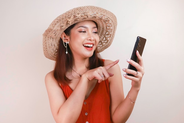 Emocionada y sonriente joven asiática señalando con el dedo el smartphone en la mano