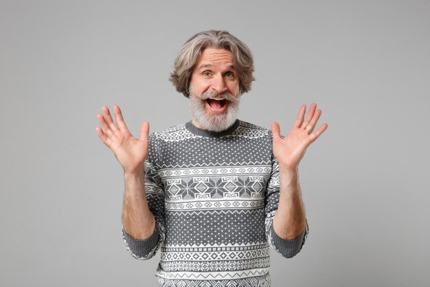 Emocionado anciano de pelo gris con bigote barbudo en suéter de punto posando aislado en fondo gris, retrato de estudio. Gente emociones sinceras concepto de estilo de vida. Simulacros de espacio de copia. Extendiendo las manos.