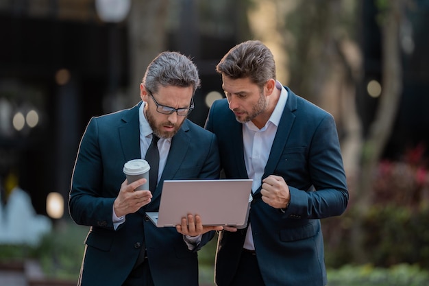 Emocionado y apuesto hombre de negocios con trajes trabajando en una computadora portátil y comunicándose con proyectos de negocios en