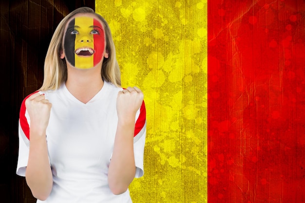Foto emocionado fanático de bélgica con pintura facial animando contra la bandera de bélgica en efecto grunge