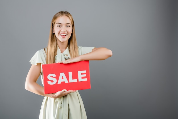 Emocionado feliz hermosa mujer joven con cartel de venta aislado sobre gris