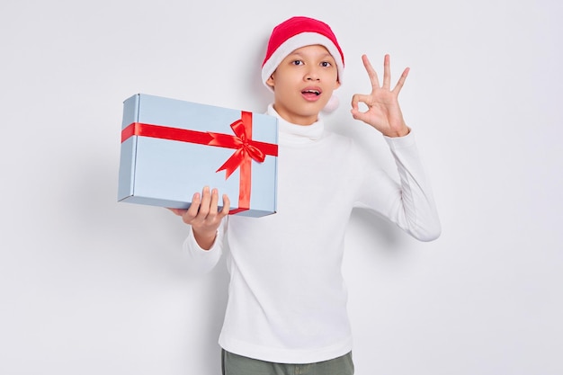 Emocionado hombre asiático con sombrero de navidad sosteniendo una caja de regalo mostrando un gesto bien aislado de fondo blanco