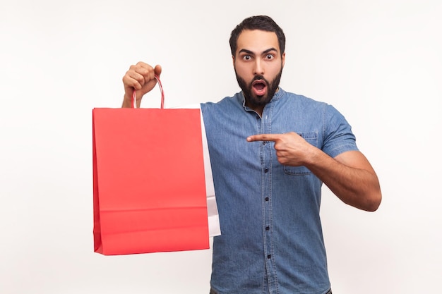 Emocionado hombre barbudo mostrando bolsas de papel de colores sorprendido con buenas compras y gran venta impactado con los precios Estudio interior aislado en fondo blanco