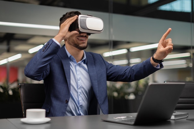 Emocionado hombre de negocios sentado en el escritorio usando gafas vr en la oficina