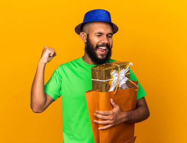 Emocionado joven afroamericano con sombrero de fiesta sosteniendo cajas de regalo mostrando gesto de sí