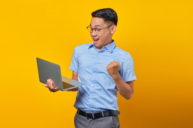 Emocionado joven asiático asiático en gafas usando laptop aislado sobre fondo amarillo hombre de negocios y empresario concepto