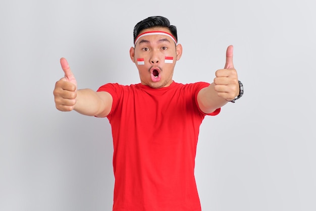 Emocionado joven asiático celebrando el día de la independencia de Indonesia mostrando Thumbs up gesto aislado sobre fondo blanco.