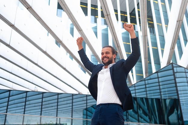 Emocionado joven empresario en traje celebrando la victoria con los brazos levantados