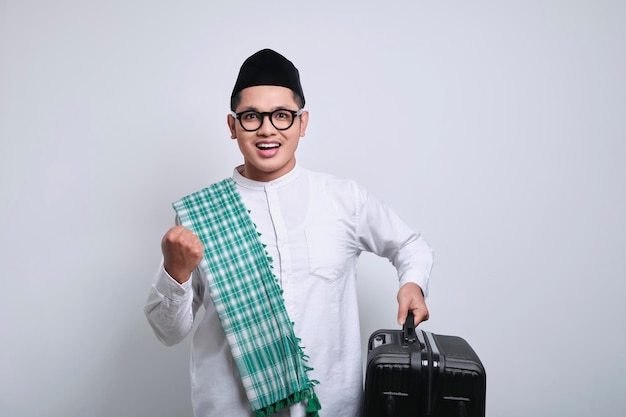 Emocionado joven musulmán asiático sosteniendo una maleta en la mano celebrando el éxito y listo para la festividad eid Mubarak