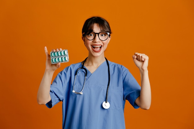 emocionado mostrando sí gesto sosteniendo píldoras joven doctora vistiendo uniforme fith estetoscopio aislado sobre fondo naranja