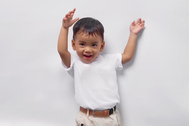 Emocionado niño pequeño asiático de 2 años con una camiseta blanca levantando un puño celebrando el éxito aislado de fondo blanco