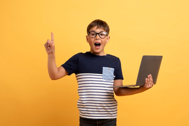 Emocionado niño preadolescente feliz sosteniendo portátil levantando el dedo