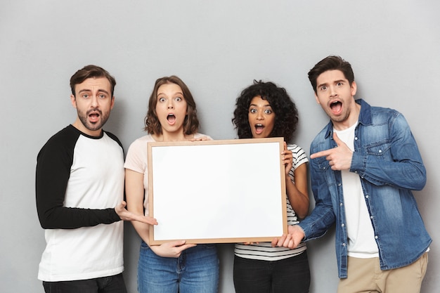 Foto emocionados amigos de parejas amorosas sorprendidas sosteniendo copyspace apuntando en blanco.