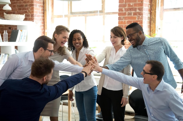 Foto emocionados colegas multirraciales dan los cinco primeros involucrados en la actividad de formación de equipos en la reunión de trabajadores diversos felices se unen para celebrar el éxito o ganar mostrar espíritu de equipo y unidad concepto de cooperación