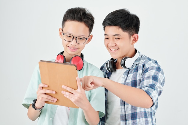 Emocionados muchachos adolescentes asiáticos discutiendo nueva aplicación en tablet PC