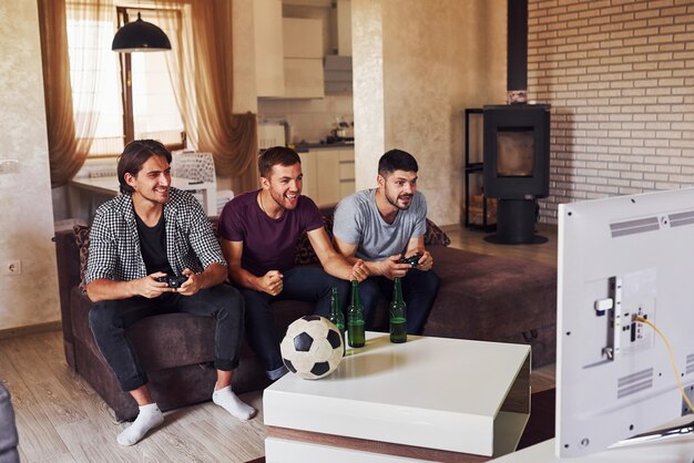 Emocionados tres amigos viendo fútbol en la televisión en casa juntos.