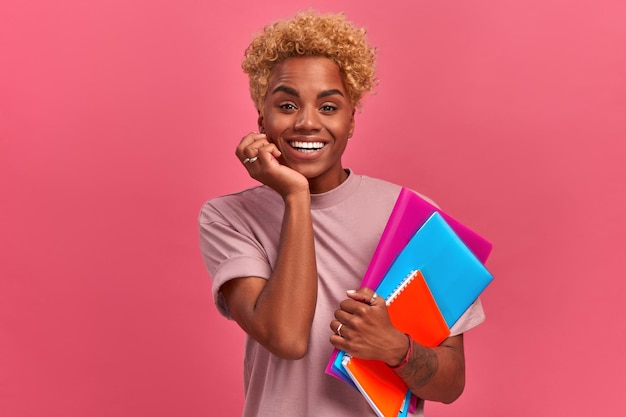 Emocional alegre joven estudiante afroamericana sosteniendo cuadernos