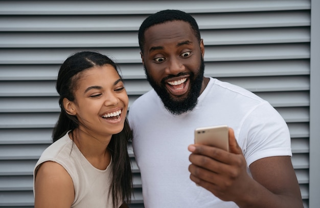 Emocional hombre afroamericano y mujer sosteniendo teléfono móvil, compras en línea