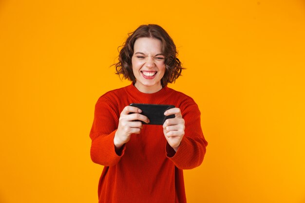 emocional jovem bonita posando isolada em jogos de parede amarela pelo telefone móvel.