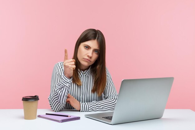 Emocional jovem sentada e trabalhando no escritório com fundo rosa