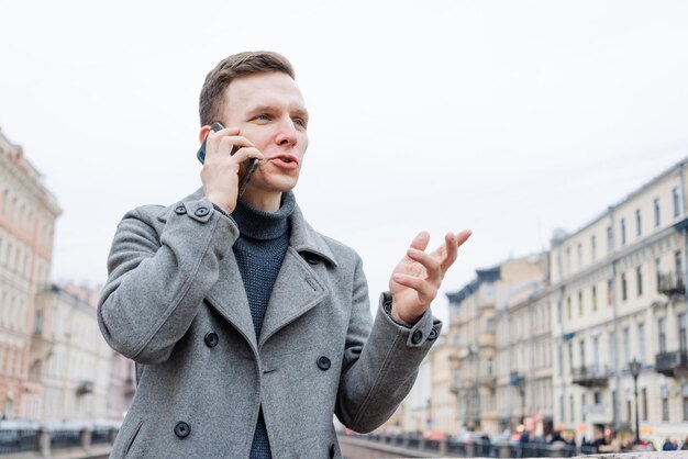 Emocional joven a través de teléfono móvil con un elegante puesto de abrigo gris