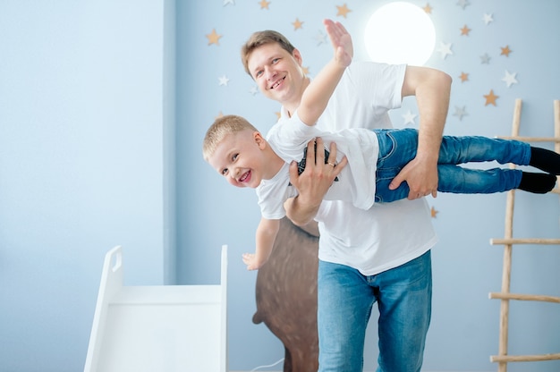 Emocional padre cría a su hijo, representando un avión volando en una habitación luminosa para niños