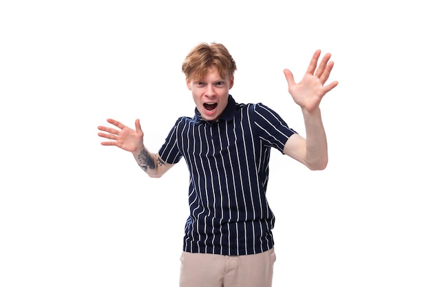 Emocional positivo hombre rubio de un año de edad con tatuajes en un polo a rayas posando sobre un fondo blanco