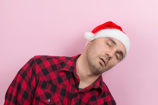 Emociones en la cara, cansancio, resaca festiva, conciencia. Un hombre en un conejo a cuadros y un sombrero rojo de Navidad