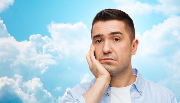Las emociones y el concepto de la gente: la cara aburrida de un hombre de mediana edad sobre el cielo azul y el fondo de las nubes