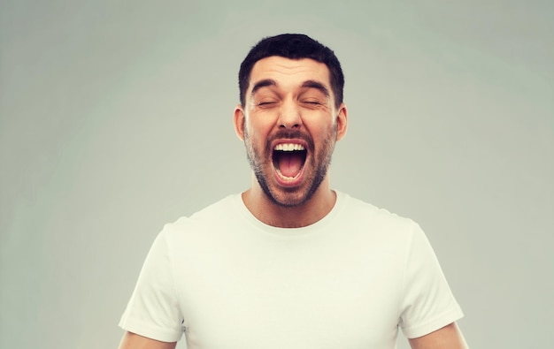 emociones, estrés, locura y concepto de la gente - hombre loco gritando en camiseta sobre fondo gris