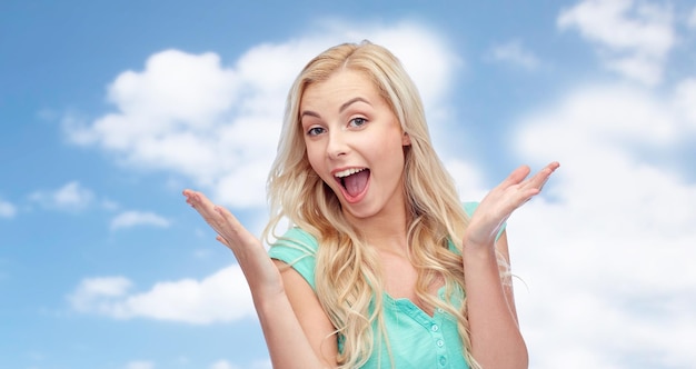 emociones, expresiones y concepto de la gente - sorprendida mujer joven sonriente o adolescente sobre el cielo azul y el fondo de las nubes